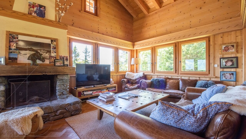 Salon chaleureux en bois avec cheminée et grandes fenêtres – Chalet Le Varouet à vendre - Verbier
